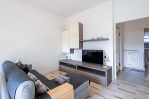 Un salon moderne avec un canapé, un téléviseur, des étagères intégrées et une vue sur l’extérieur.