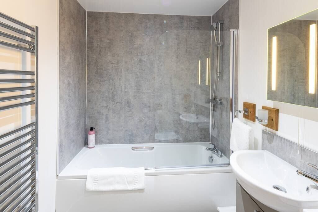 A modern bathroom with a glass-enclosed shower, a white bathtub, and a large mirror with integrated lighting.