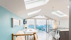A modern apartment with a dining area, kitchen, and a balcony with a city view. - Seaside 3BD Retreat with Balcony and Stunning Views (Westward Ho!)