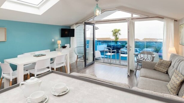 A modern room with a dining area, a sofa, and a balcony with a pool view. - Seaside 3BD Retreat with Balcony and Stunning Views (Westward Ho!)