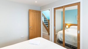 A hotel room with a bed, a wooden wardrobe, a mirror, and a staircase leading to another room. - Seaside 3BD Retreat with Balcony and Stunning Views (Westward Ho!)