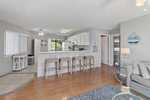 A modern kitchen with white cabinets, a bar area with stools, a ceiling fan, and a sign on the wall.