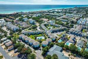 A coastal residential area with multiple-story houses, a central swimming pool, and a view of the ocean.