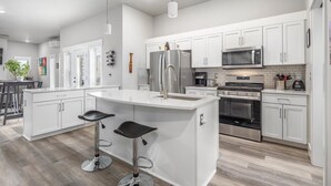 Una cocina moderna con armarios blancos, electrodomésticos de acero inoxidable y una isla central con taburetes de bar.