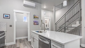 Una cocina moderna con una isla central, electrodomésticos de acero inoxidable y una escalera que sube a un nivel superior.
