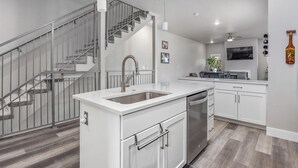 Una cocina moderna con una isla central, electrodomésticos de acero inoxidable y una escalera con barandilla de cristal.