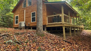 Een vakantiehuisje van hout met een balkon, omgeven door bomen en herfstbladeren.