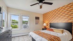 Un dormitorio con cama, cómoda, ventilador de techo y ventana con vista a un estacionamiento.