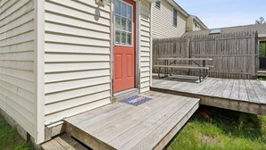 Una casa con puerta roja, terraza de madera y valla de madera.