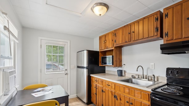 Una cocina compacta con armarios de madera, un refrigerador, un microondas, un fregadero y una estufa.