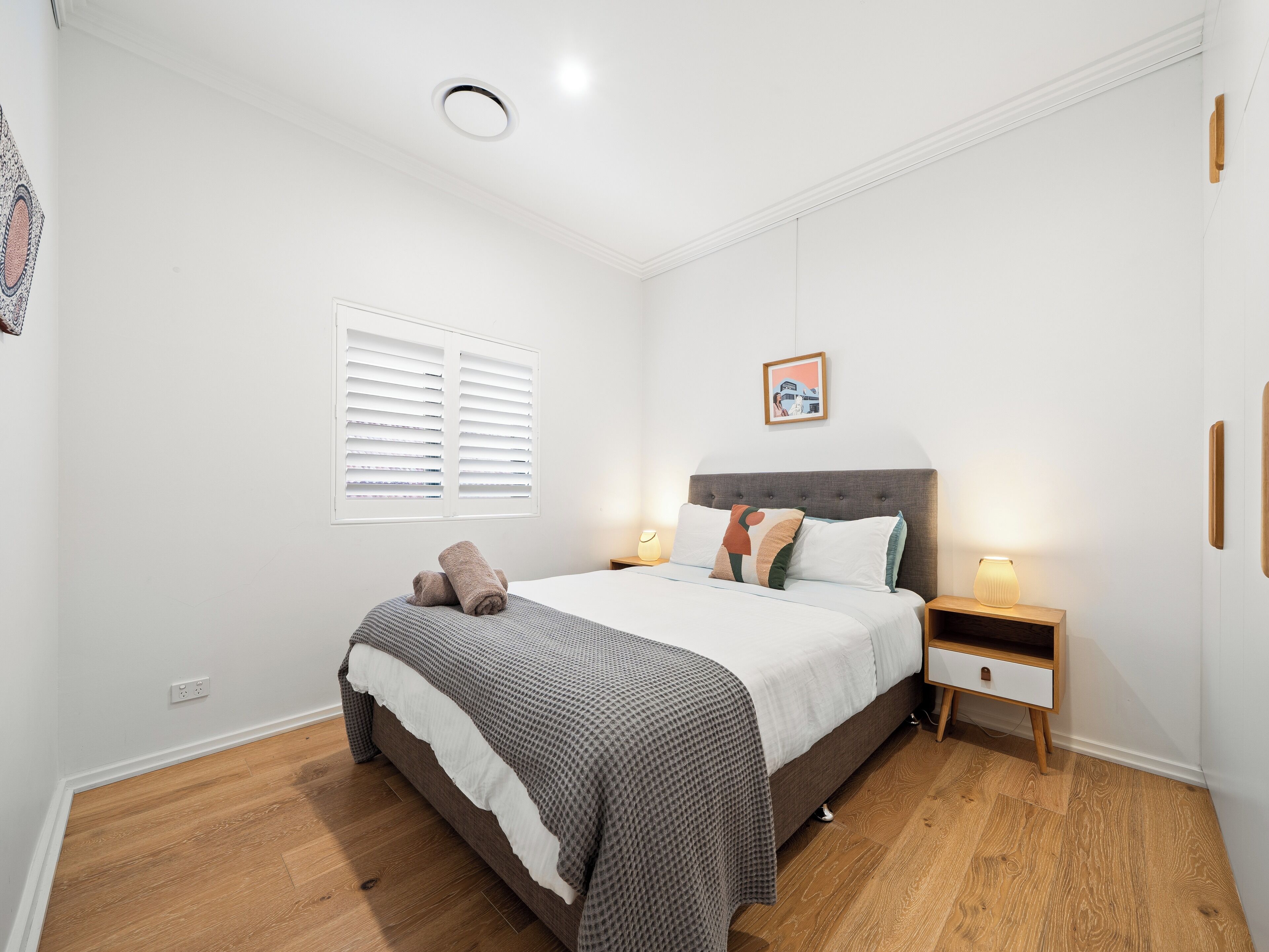 A bedroom with a bed, bedside tables, a nightstand, a wall-mounted picture, and a ceiling light.