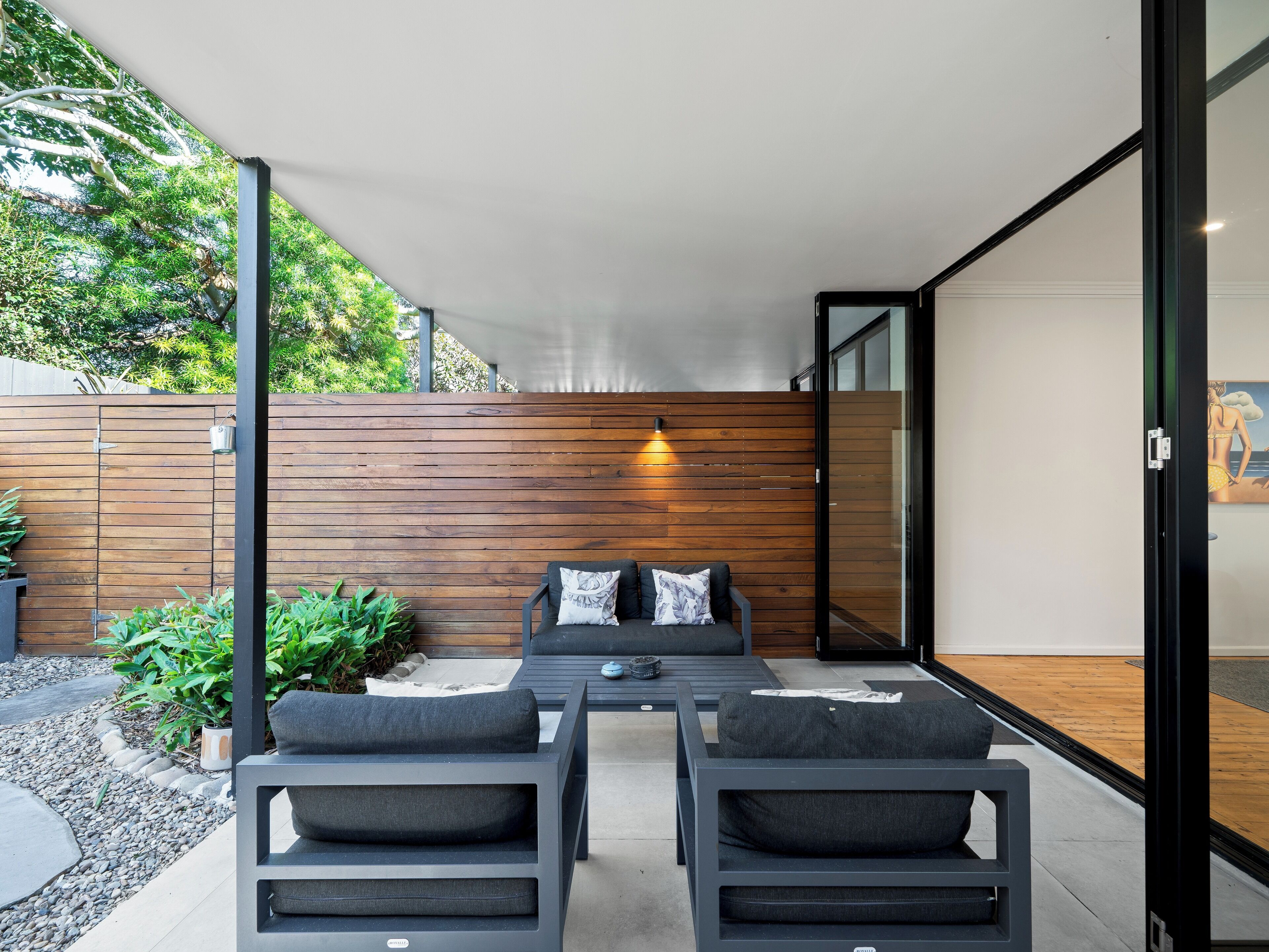 A modern outdoor patio with a wooden wall, two grey sofas, and a table.