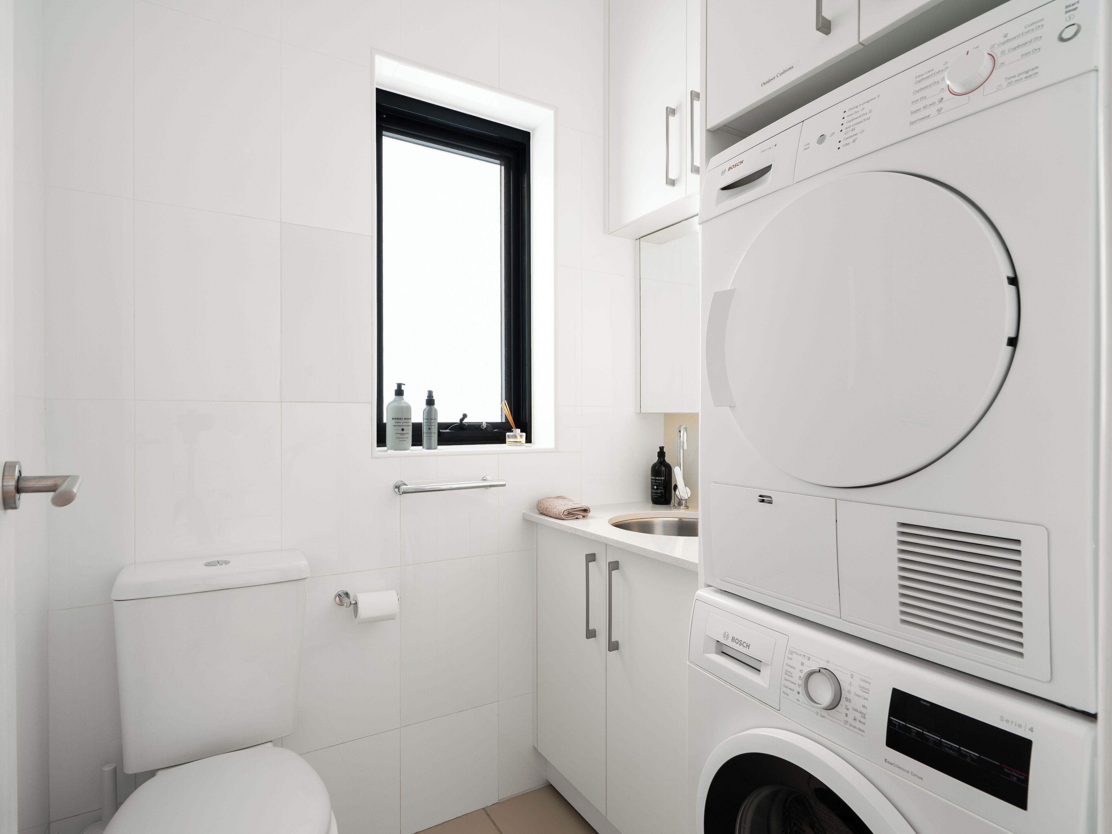 A compact, modern bathroom with a toilet, sink, and stacked washer-dryer unit.