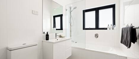 A modern bathroom with a toilet, sink, mirror, shower, and bathtub.