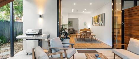 Un espace extérieur aménagé en terrasse, avec un barbecue, des sièges et une vue sur l’intérieur de la maison.