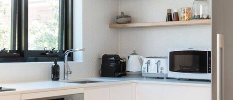 Eine moderne Küche mit weißen Schränken, einem Geschirrspüler von Bosch, einer Mikrowelle, einer Kaffeemaschine und einem Fenster mit Jalousien.