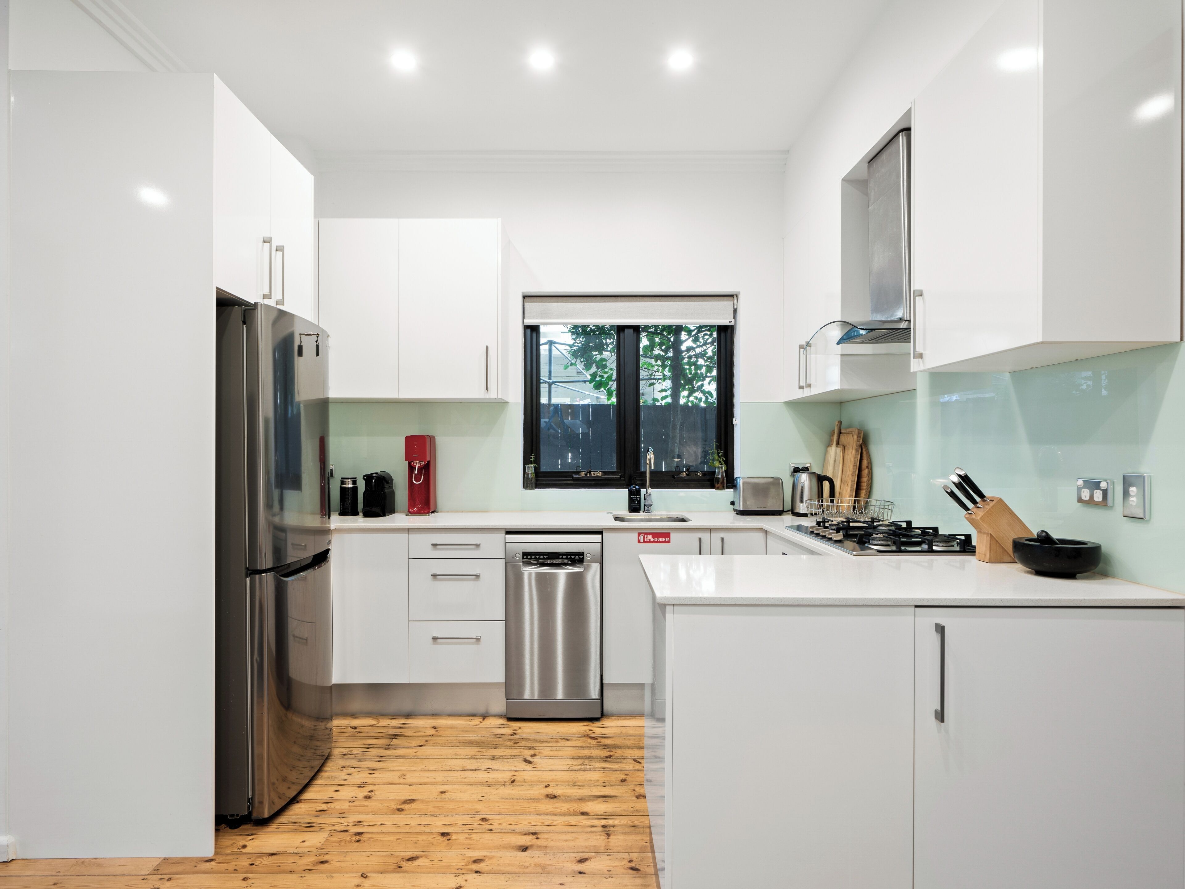 A modern kitchen with white cabinets, stainless steel appliances, and a wooden floor.