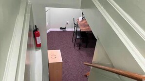 Kapeat portaat, joiden päällä on violetti matto, vasemmalla puolella palosammutin, taustalla puinen pöytä ja tuoleja sekä lattialla pahvilaatikko.