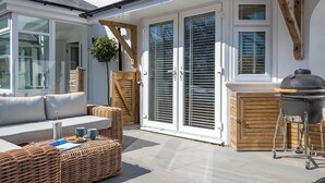 Eine Terrasse mit einem Korbsessel, einem Grill und einem Holztor.