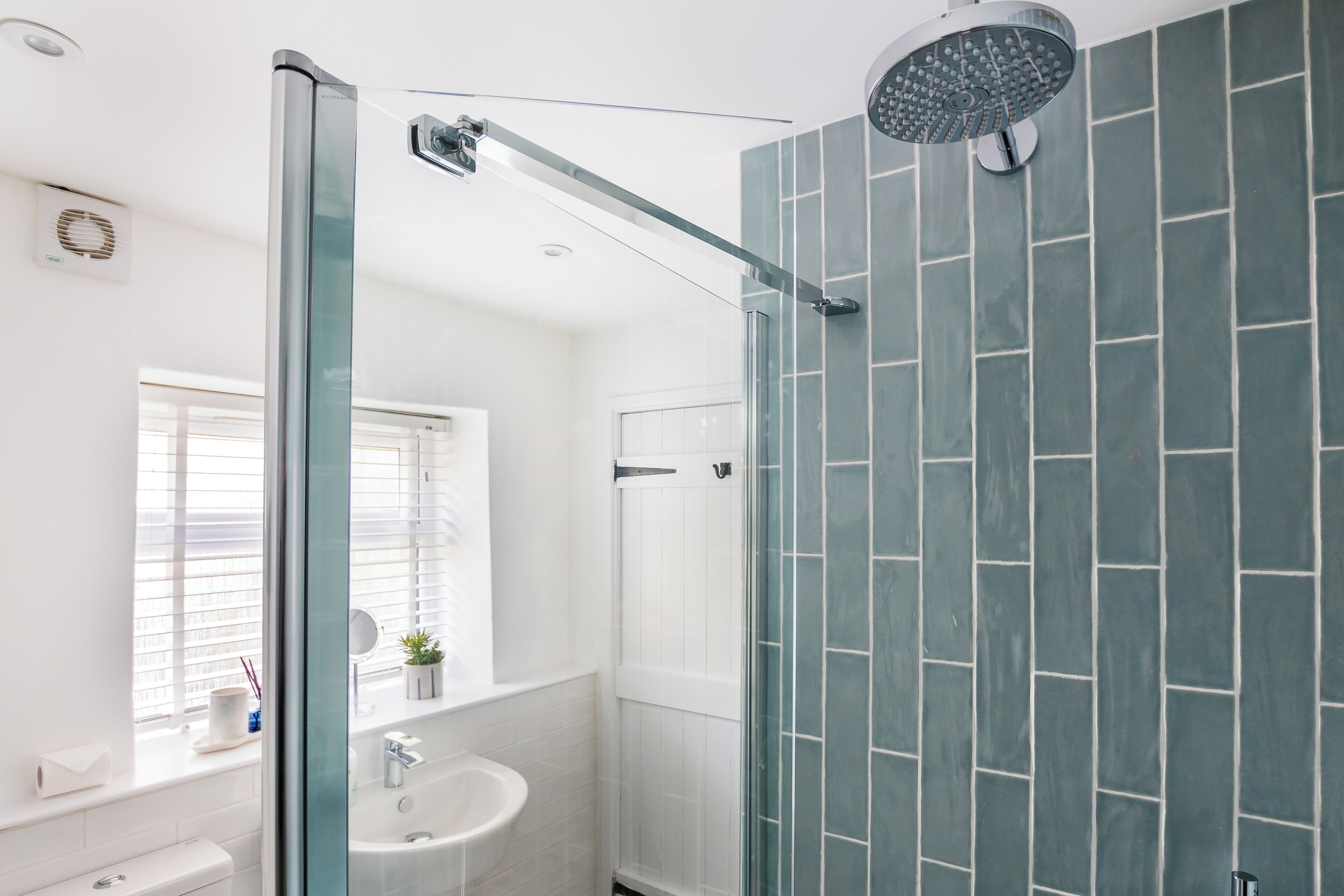 A modern bathroom with a glass-enclosed shower, a white sink, and a window with blinds.