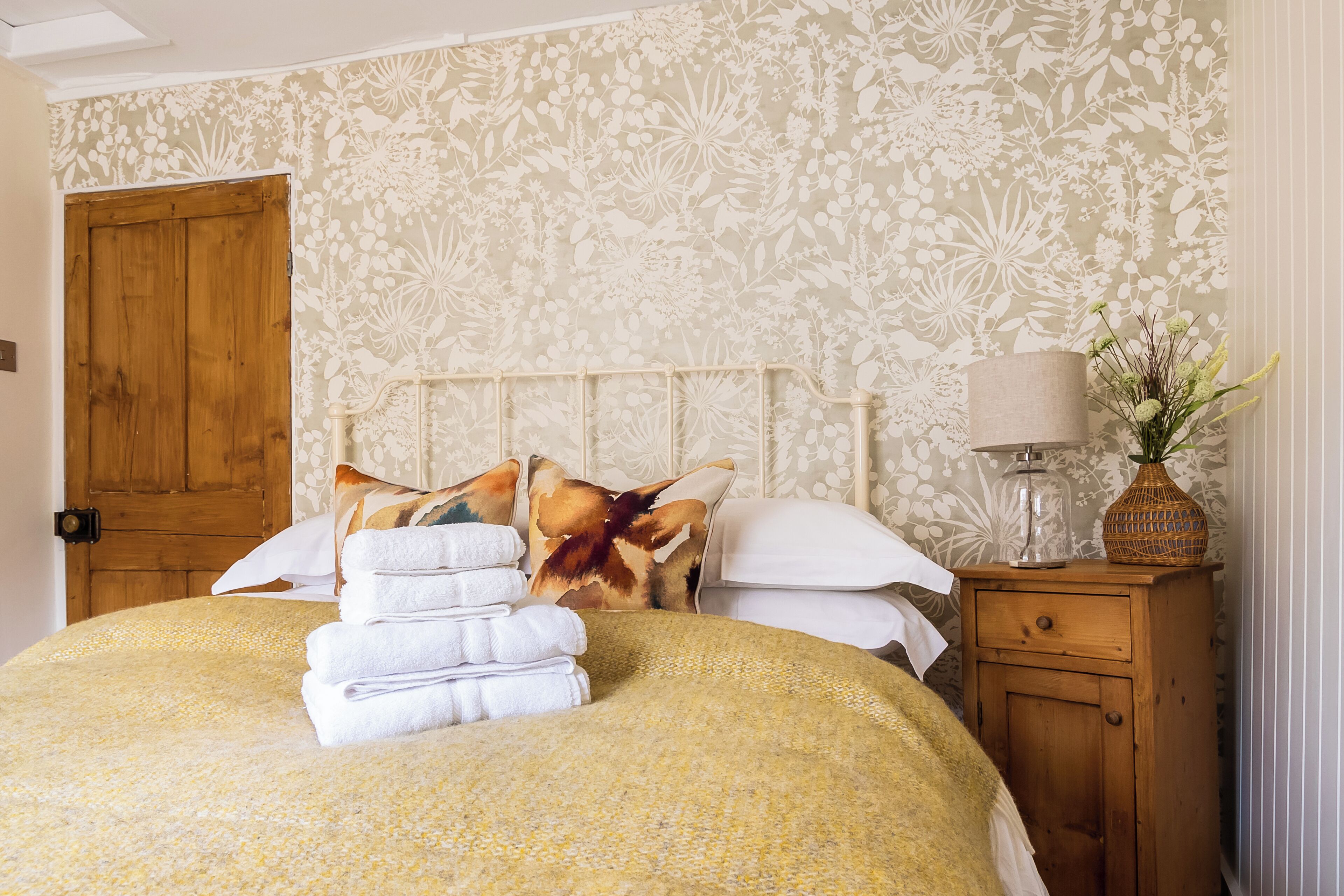 A neatly made bed with a floral bedspread and a stack of white towels.