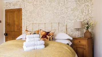 A neatly made bed with a floral bedspread and a stack of white towels.