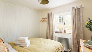A bedroom with a bed, a radiator, a window with curtains, and a wooden dresser with a vase.
