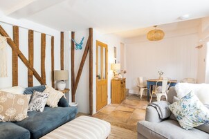 Una sala de estar acogedora con un sofá azul, un sofá gris y una estructura de pared de madera. En el fondo, hay un área de comedor con una mesa y sillas.