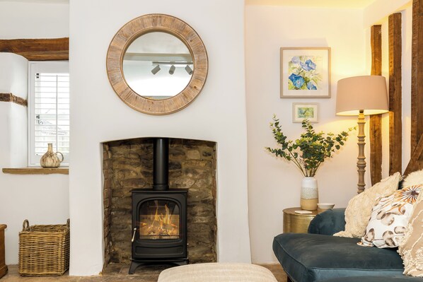 A cozy living room with a stone fireplace, a round mirror, a blue sofa, and a lamp on a side table.