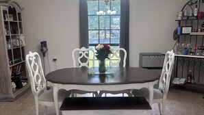 Ein Essbereich mit rundem Tisch, weißen Stühlen, einer Bank, einer Chandelierleuchtre, einem Fenster mit Blick und einem Bücherregal.