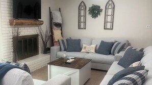 Ein Wohnzimmer mit Kamin, einer Sofagarnitur, einem Couchtisch und einem an einer Ziegelwand montierten Fernseher.