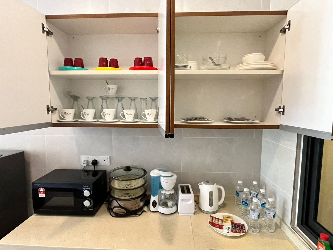 Eine Küche mit Mikrowelle, Kaffeemaschine, Wasserkocher und Wasserflaschen auf der Arbeitsfläche.