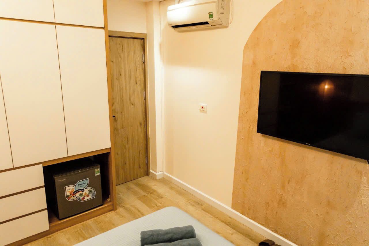 Una habitación con una cama, televisor montado en la pared, una puerta de madera y un equipo de aire acondicionado.