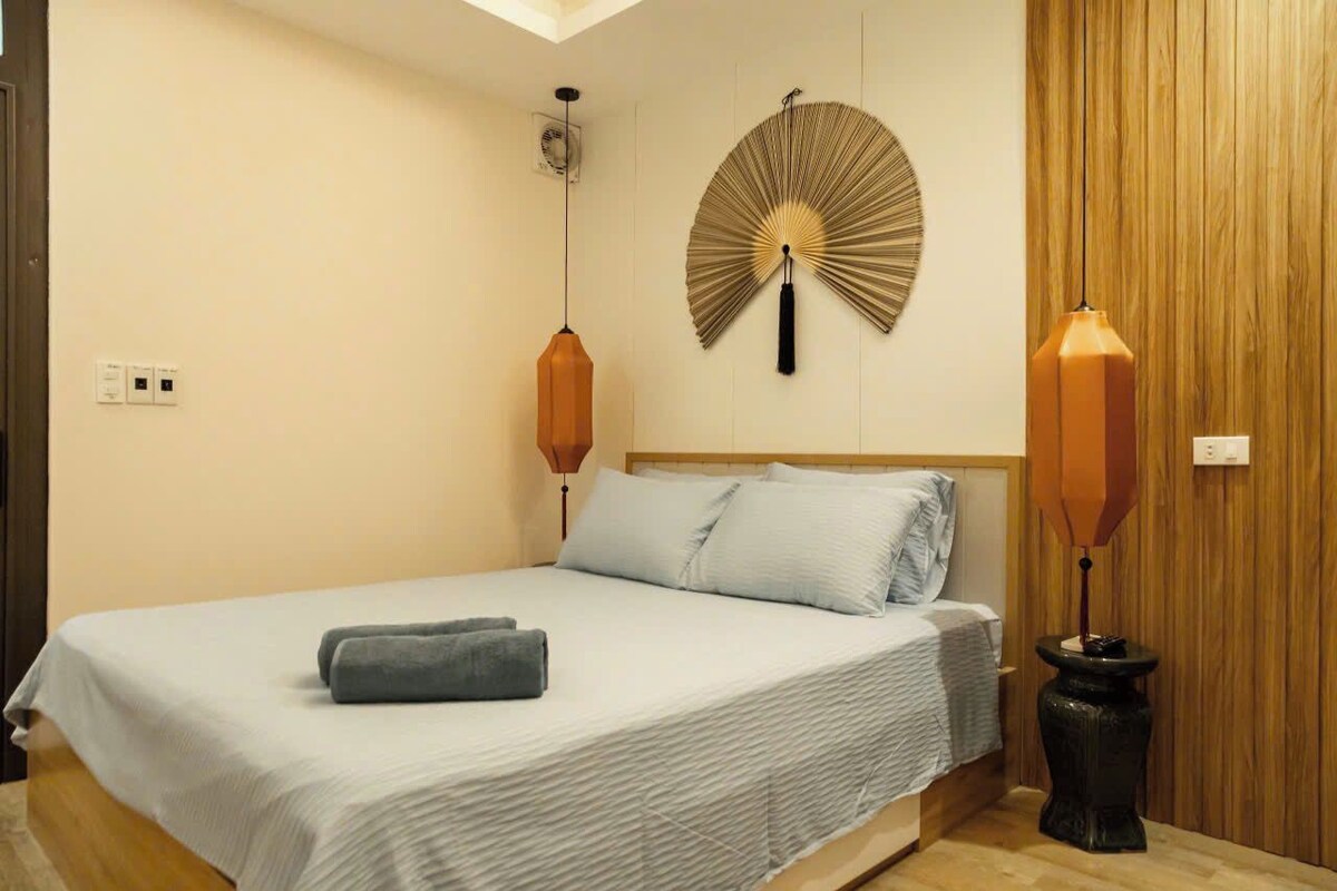 Quarto com cama, ventilador de parede e duas luminárias.