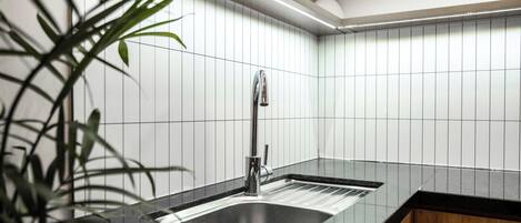 A modern kitchen with a black countertop, stainless steel sink, and white tiled backsplash.