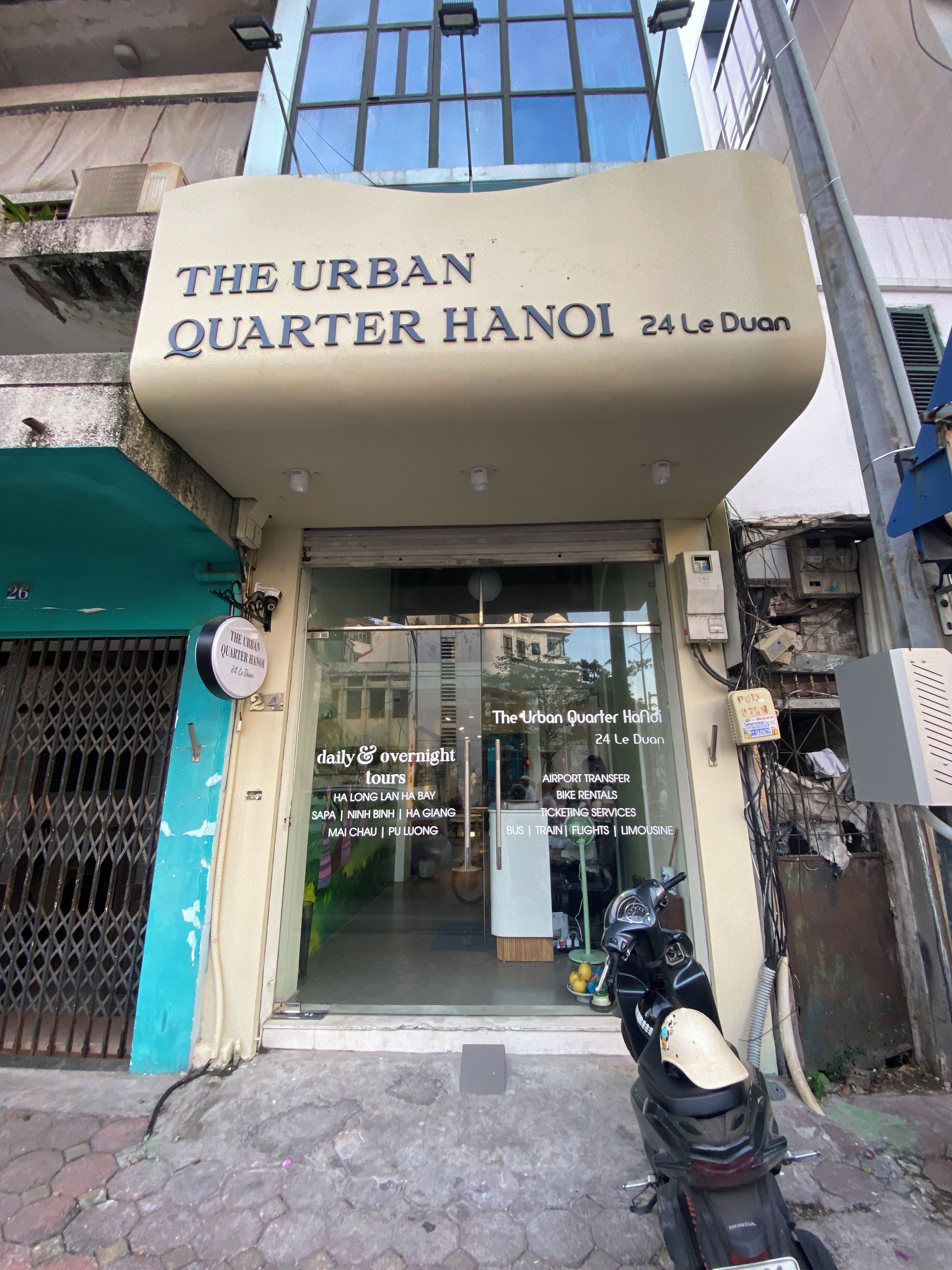 Un edifici amb un cartell que diu 'The Urban Quarter Hanoi 24 Le Duan' i una llista de serveis que inclouen visites turístiques i transport.