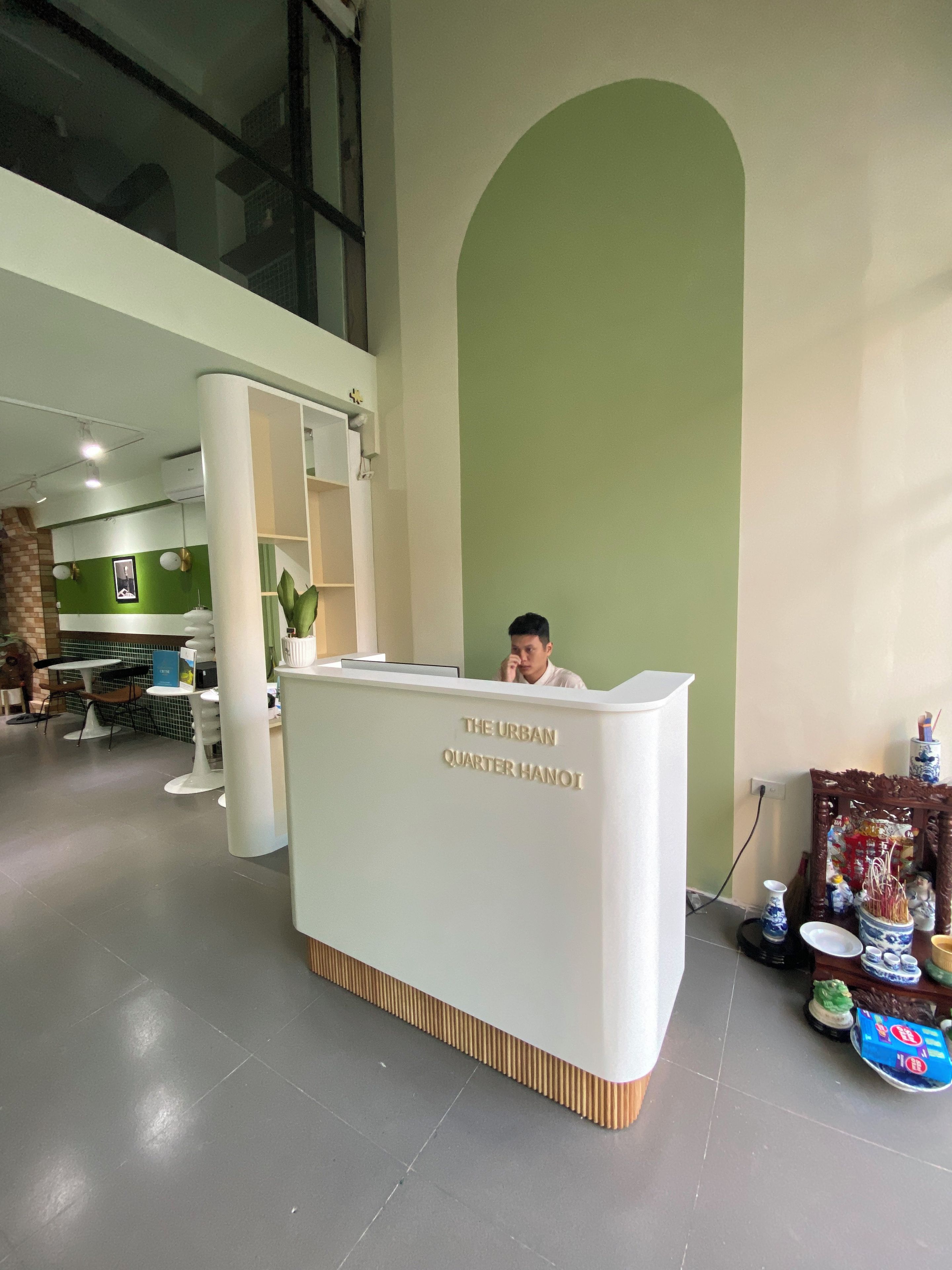 Un mostrador de recepción con el rótulo 'The Urban Quarter Hanoi' y una persona sentada detrás.