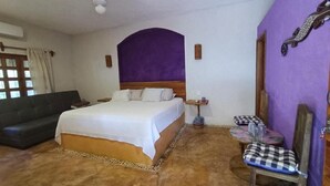Ein Hotelzimmer mit Bett, Sofa, Sessel, einem kleinen Tisch und einer lilafarbenen Akzentwand.