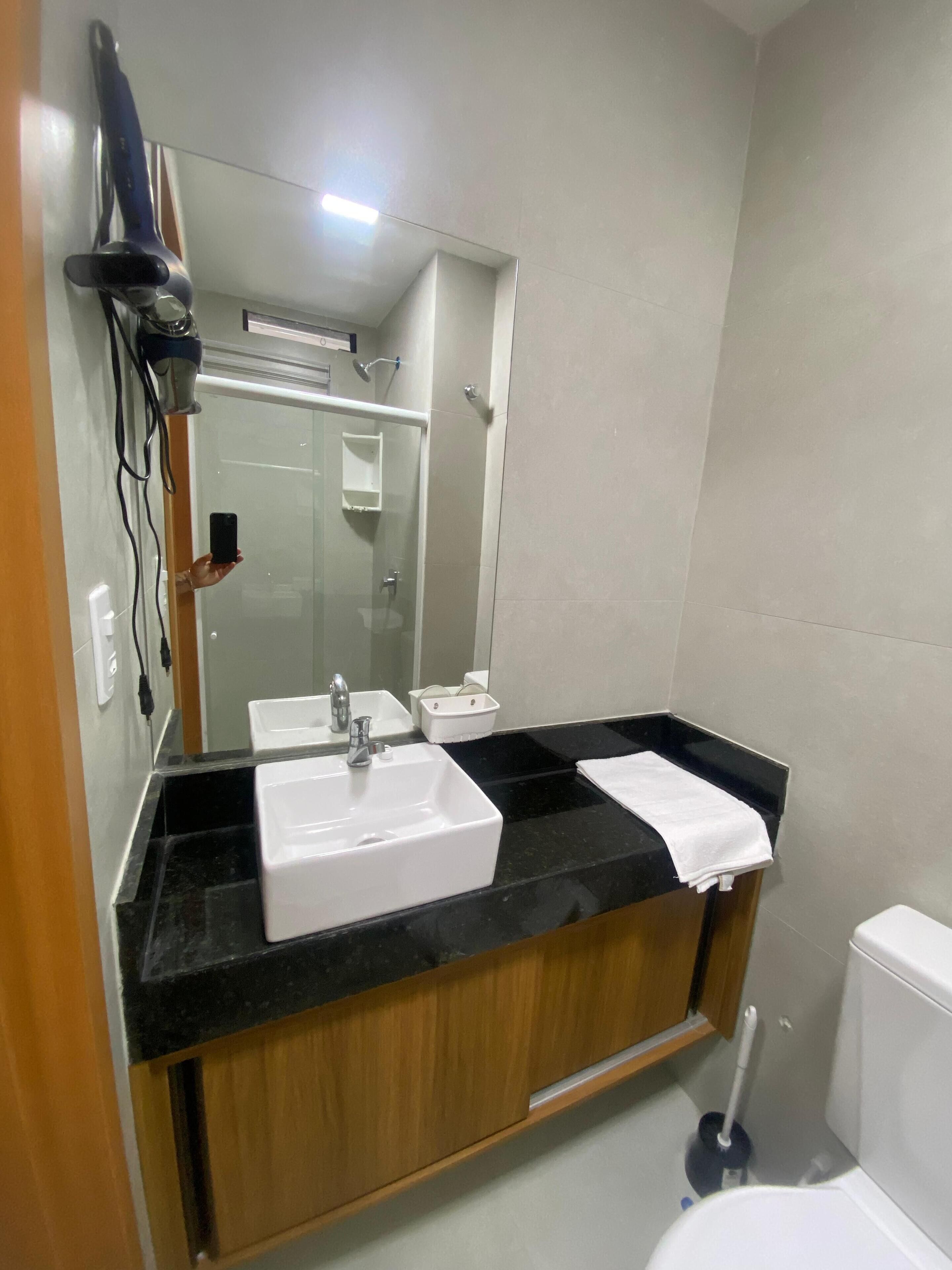 A bathroom with a black countertop, two sinks, a mirror, and a toilet.