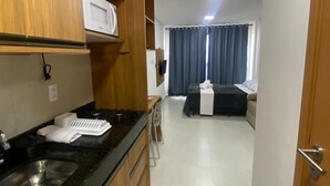 Eine kompakte Küche mit Mikrowelle, Spüle und Herd. Es gibt einen Essbereich mit Tisch und Stühlen sowie ein Schlafzimmer mit Bett und Vorhängen.