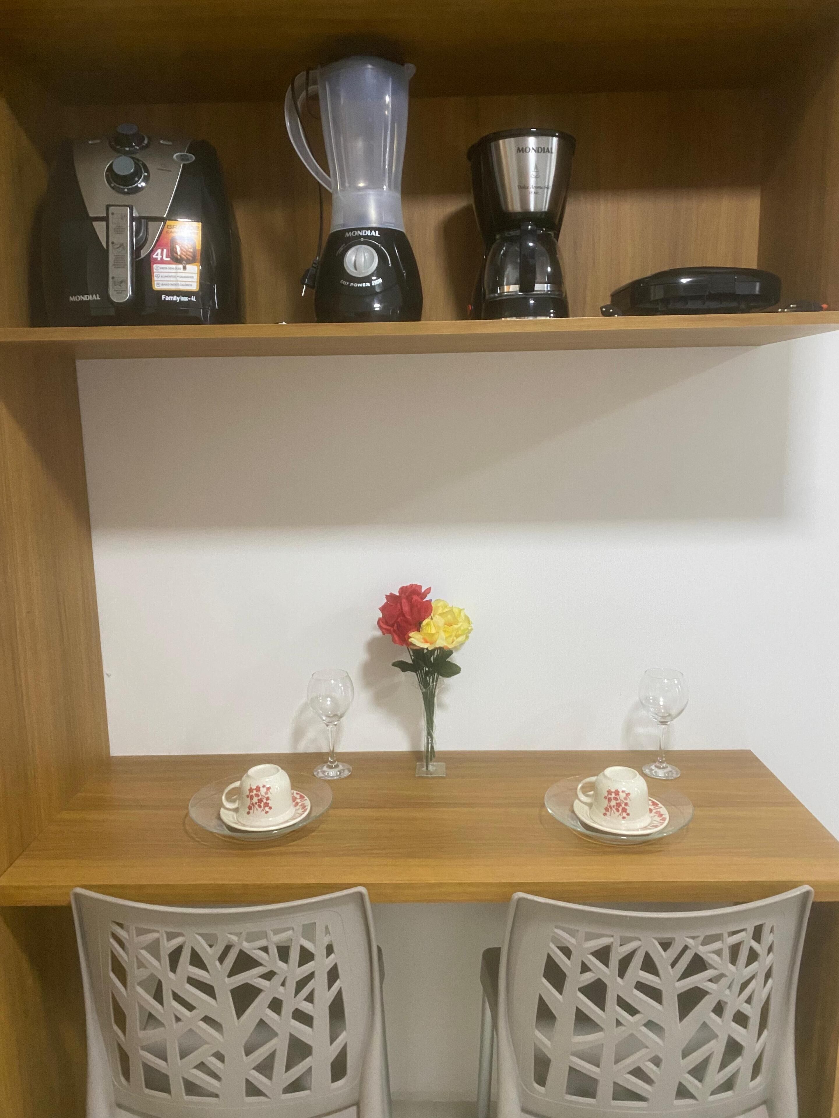 A kitchen with a wooden countertop, two chairs, a vase with flowers, and kitchen appliances on the shelf above.