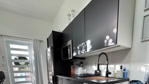 Una cocina moderna con gabinetes negros, un microondas y un lavamanos. En la encimera, hay una cesta de mimbre con una toalla roja y una bolsa azul.