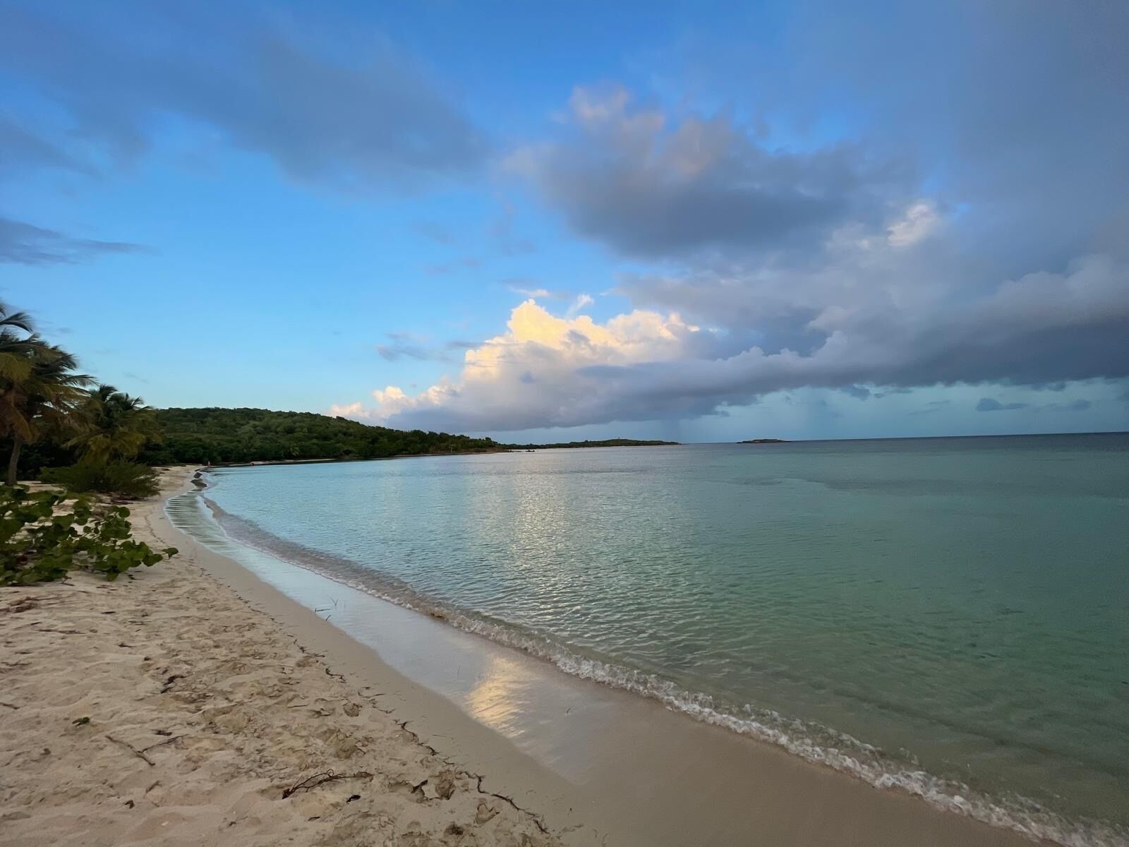 A beach with clear water, a sandy shore, and a distant island.