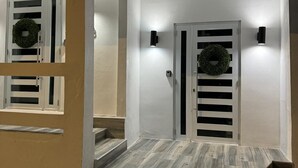 Una entrada de edificio moderna con fachada blanca, escalera de madera y dos puertas adornadas con coronas.