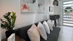 Una sala de estar moderna con un sofá gris oscuro, arte abstracto en la pared, una planta en maceta y un comedor con una silla y mesa negros.