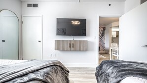 A modern bedroom with two beds, a TV mounted on the wall, and a wooden cabinet below it.