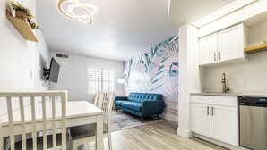 A modern kitchen with white cabinets, a built-in dishwasher, and a blue sofa in the living area.