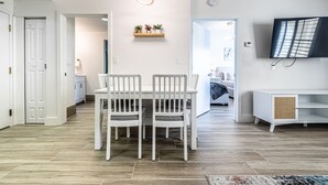 A modern living room with a dining area, white furniture, a flat-screen TV, and a wooden floor.