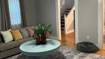 Un salon avec une table basse ronde, un ventilateur de plafond, un canapé avec des coussins, une plante et un tapis.