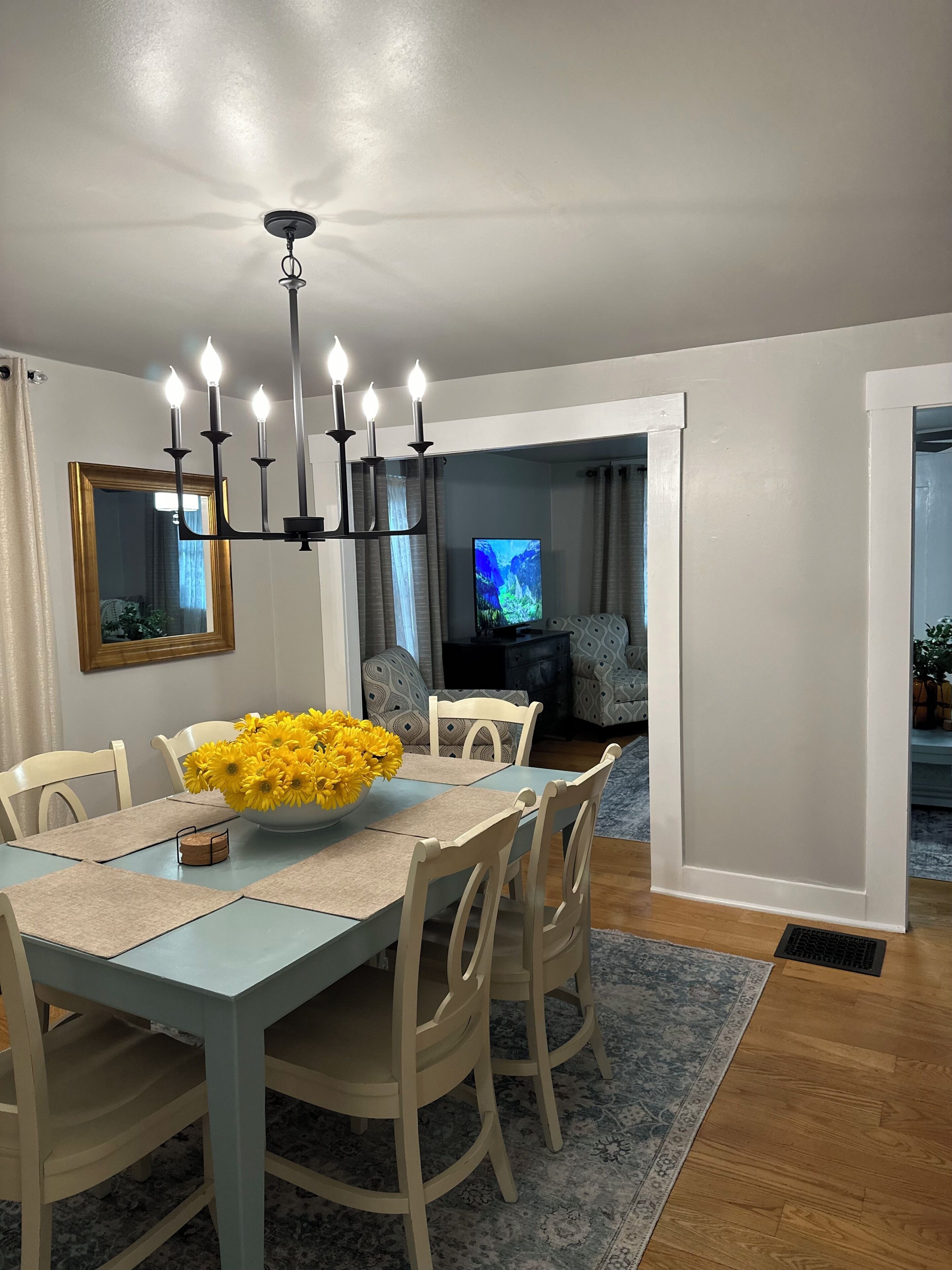 A dining area with a table set for four, a chandelier, and a television in the background.